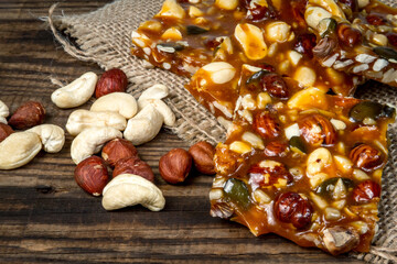 A sweet and healthy homemade snack, featuring nuts, hazelnuts, and pumpkin seeds in caramel. Old boards and a burlap sack serve as the backdrop for this food photography.