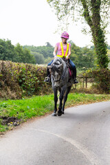 Young female rider and her dapple grey horse riding out in the English countryside on a summers day. The girl is wearing reflective clothing to be seen and be safe on the roads.