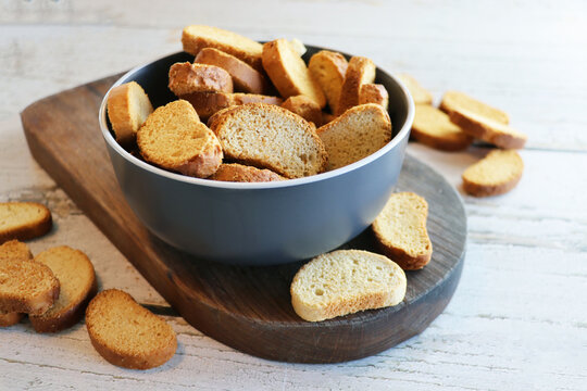 Crispy rusks in bowl on wooden table, closeup