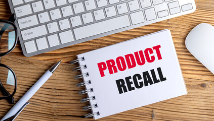 PRODUCT RECALL text on spiral notepad with keyboard, mouse, glasses and pen on wooden desk