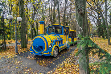 Tourist park train under tall trees autumn colors community recreation theme family friendly transport nostalgic vibe