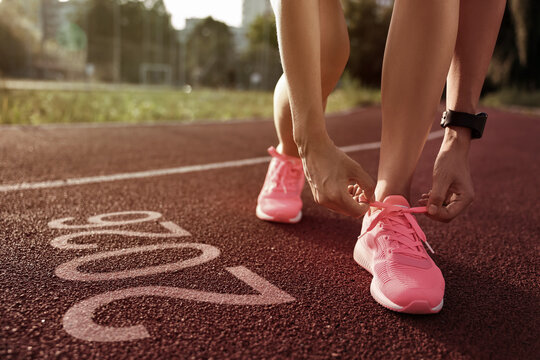 New Year. Woman tying shoelaces near numbers 2026 on road at stadium, closeup - Powered by Adobe