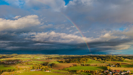 Bunte Regenbogenlandschaft &uuml;ber gr&uuml;nen Feldern und D&ouml;rfern im Herbst