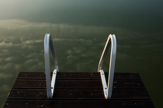 Wooden Dock with Metal Ladder Handrails Leading into Calm, Reflective Water