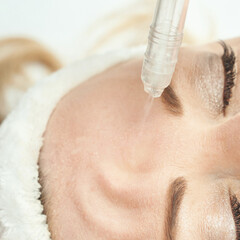 Naklejka premium Caucasian female receiving facial treatment with microdermabrasion for skincare and rejuvenation.