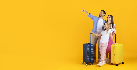 Smiling family standing with suitcases on yellow background and pointing at copy space. Parents and daughter ready for vacation, symbol of travel, adventure, and excitement, panorama