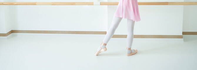 Young caucasian female ballet dancer practicing at barre in pink dress and pointe shoes in bright...