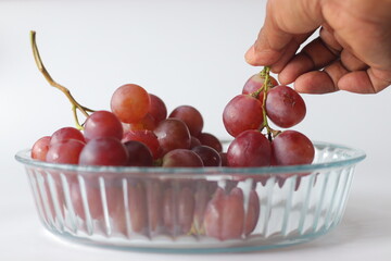 A hand reaching to a glass bowl of Red table grapes or Red Globe, Crimson Seedless or Flame Seedless