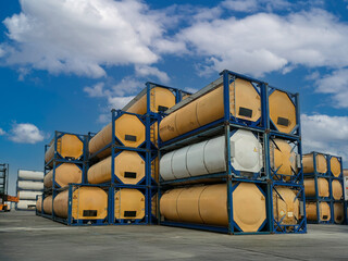Stack of Isotank containers in logistics terminal. Cylindrical chemical and liquid transport tanks arranged in multiple layers at an outdoor industrial depot. 