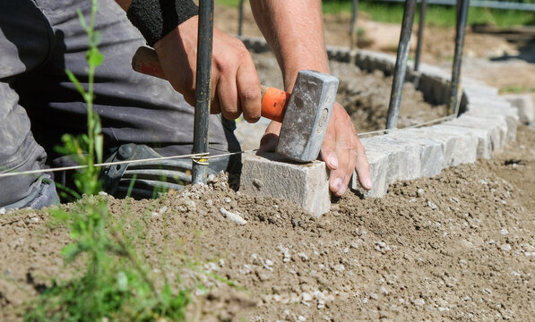 Landschaftsgärtner bei der Arbeit im Detail – präzise Handarbeit im Gartenbau mit Fokus auf Steine, Werkzeug und Struktur. Selektive Schärfe, viel Copy Space