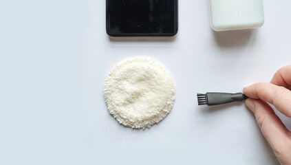 Cleaning accessories with hand holding brush near smartphone, cotton pad, and bottle on white...