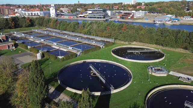 Wastewater Treatment Plant with purification basins. City skyline and modern harbor development in the background under a sunny autumn sky