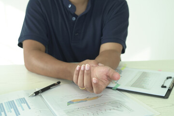 Young asian businessman is suffering pain on wrist, finger and arm, arthritis inflammation while working and he is massaging himself and doing exercise with his hands to relax and to relieve pain.
