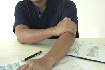 Young asian businessman is suffering pain on wrist, finger and arm, arthritis inflammation while working and he is massaging himself and doing exercise with his hands to relax and to relieve pain.
