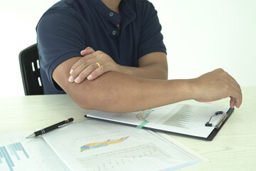 Young asian businessman is suffering pain on wrist, finger and arm, arthritis inflammation while working and he is massaging himself and doing exercise with his hands to relax and to relieve pain.
