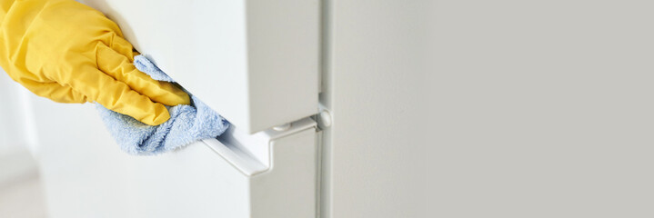 Close-up of gloved hand cleaning refrigerator handle with blue cloth for hygiene.