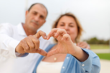 Obraz premium A man and woman, an older couple, make a heart with their hands.