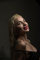 Blonde woman with wet hair poses elegantly in a dimly lit room, showcasing beauty and confidence, with soft shadows enhancing her features and creating a captivating atmosphere