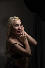 Blonde woman with wet hair poses elegantly in a dimly lit room, showcasing beauty and confidence, with soft shadows enhancing her features and creating a captivating atmosphere