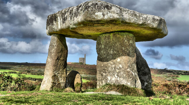 Beautiful and dramatic image of neolithic structure (Lanyon Quoit) in Cornwall with dramatic sky and with engine house of Ding Dong Mine framed by the quoit