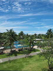 Fototapeta premium High-Floor Hotel Balcony View of Sky, Tropical Trees, Walkways, and Swimming Pool at Luxury Resort in Phuket Thailand