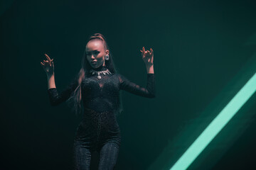 Elegant gogo dancer on nightclub stage, poised gesture under soft teal light—confidence, grace and attitude; horizontal frame with clean right-side negative space and a diagonal light beam.