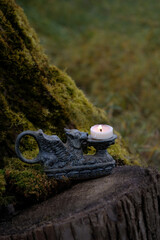 vintage candle holder in shape of a winged lion with burning candle outdoor, nature background. mystery fairy tale scene. esoteric ceremony. witchcraft, magic ritual with candle