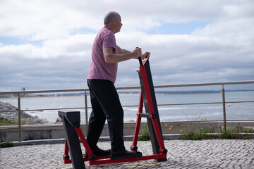 Elderly man exercising on outdoor fitness equipment by the ocean in Portugal, healthy lifestyle