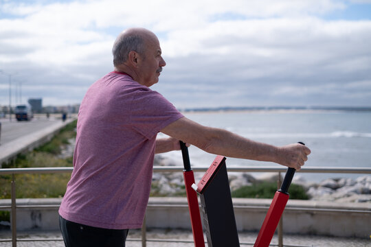 Elderly man exercising on outdoor fitness equipment by the ocean in Portugal, healthy lifestyle - Powered by Adobe