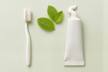White toothbrush, mint leaves and toothpaste on pastel background
