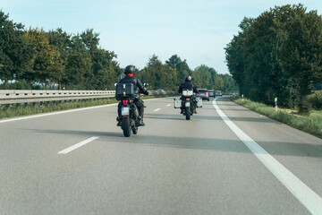 Motorcycles riding on a highway surrounded by trees during a clear afternoon