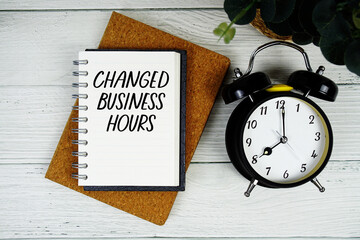 Changed Business Hours text written on notepad with alarm clock on wooden background