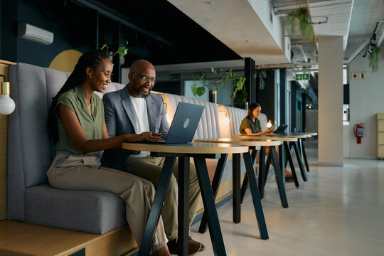 Happy black businessman and businesswoman working on laptop sitting at desk in office lounge
