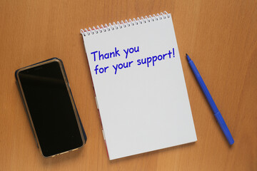 Open notebook with inscription: Thank you for your support, mobile phone and marker on table