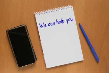 Open notebook with inscription: We can help you, mobile phone and marker on table