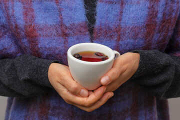 A woman dressed in warm clothing holds a cup of rosehip tea. Concept of warming up during the cold season.