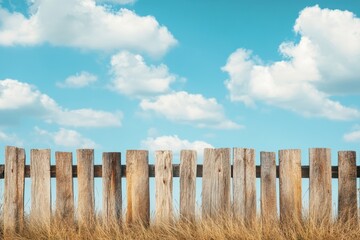 Rustic wooden fence under a bright blue sky with fluffy clouds and tall grass in the background