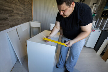 Man measuring and marking kitchen cabinet components with a ruler and pencil during a home...