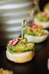 Elegant avocado canapes with pistachios and edible flower on black serving tray