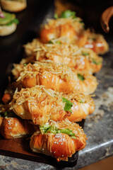 Golden croissant sandwiches with crispy onions and sesame seeds on dark serving tray