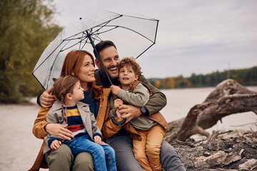 Happy family under umbrella enjoying in autumn day in nature. © Drazen