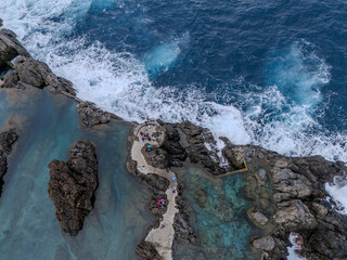 Obraz premium Aerial view of natural lava pools and coastal village in Porto Moniz, Madeira, surrounded by dramatic cliffs and Atlantic waves. 