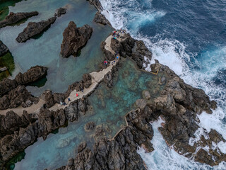 Aerial view of natural lava pools and coastal village in Porto Moniz, Madeira, surrounded by dramatic cliffs and Atlantic waves.
