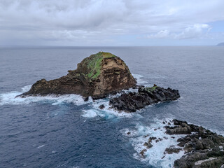 Fototapeta premium Natural volcanic swimming pools surrounded by rugged lava rocks in Porto Moniz, Madeira, with a scenic ocean backdrop and a small island offshore. 