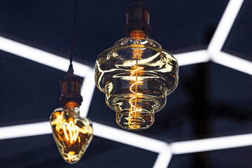 A decorative incandescent light bulb hangs from a dark ceiling.