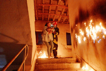 Fototapeta premium Two brave firefighters helping a frightened woman carrying her cat to safety from a burning building, symbolizing heroism, compassion, and teamwork during an emergency rescue operation.