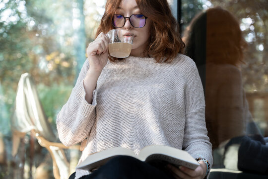 Young redhead woman drinking tea while reading a book outside her cabin - Powered by Adobe