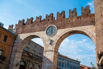The historic Portoni della Bra in Verona Italy with two large stone arches, a crenelated walkway, and a prominent central clock