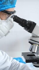 Medical scientist senior man wearing protective mask, glasses and bouffant cap using microscope doing scientific research in a laboratory. Medicine and science concept