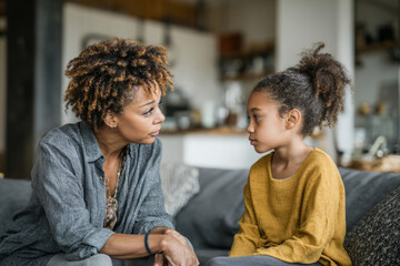 Woman and girl sitting on couch at home and having a serious conversation